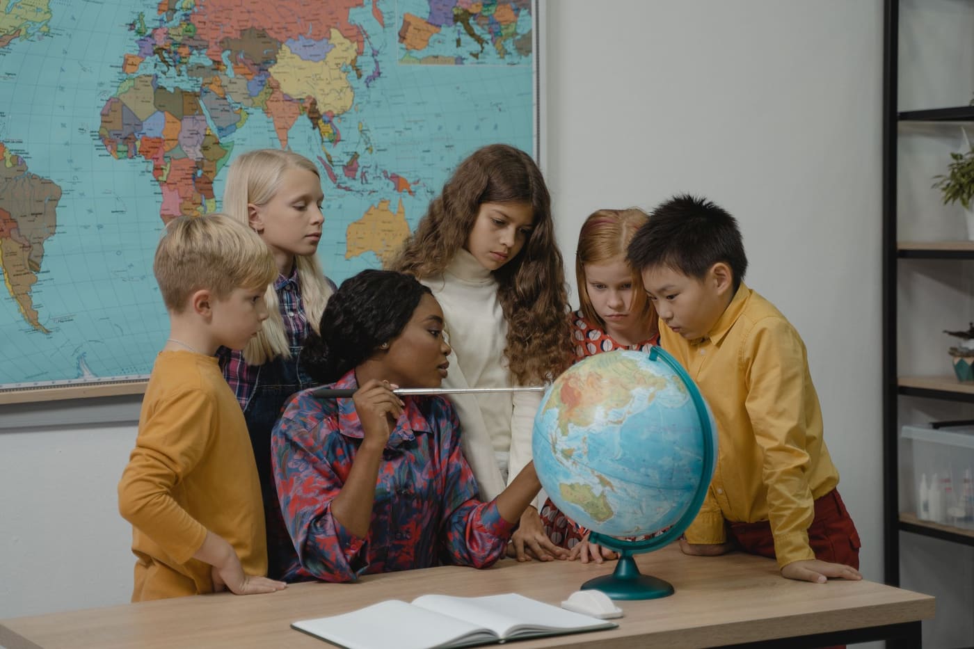 Une enseignante et un groupe d’enfants réunis autour d’un globe pendant une activité pédagogique en classe.