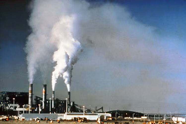 Vue historique d’un site industriel avec des cheminées et des panaches dans le ciel Vue historique d’un site industriel avec des cheminées et des panaches dans le ciel.