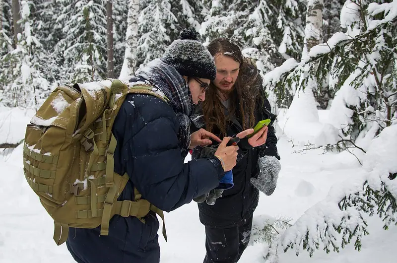 Deux personnes consultent leurs appareils de navigation dans une forêt enneigée.